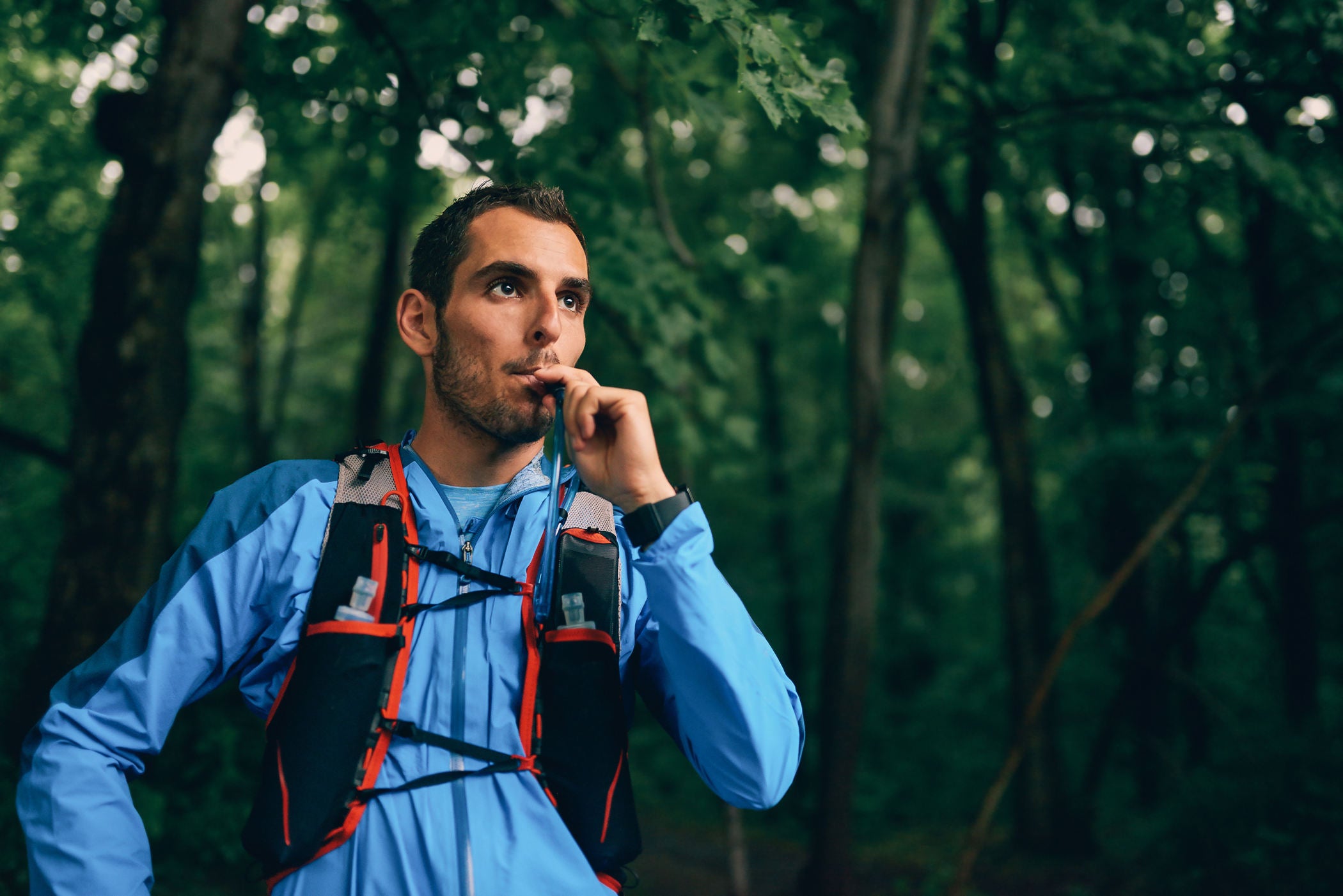 Athletic young man drinking water in the forest during a hike