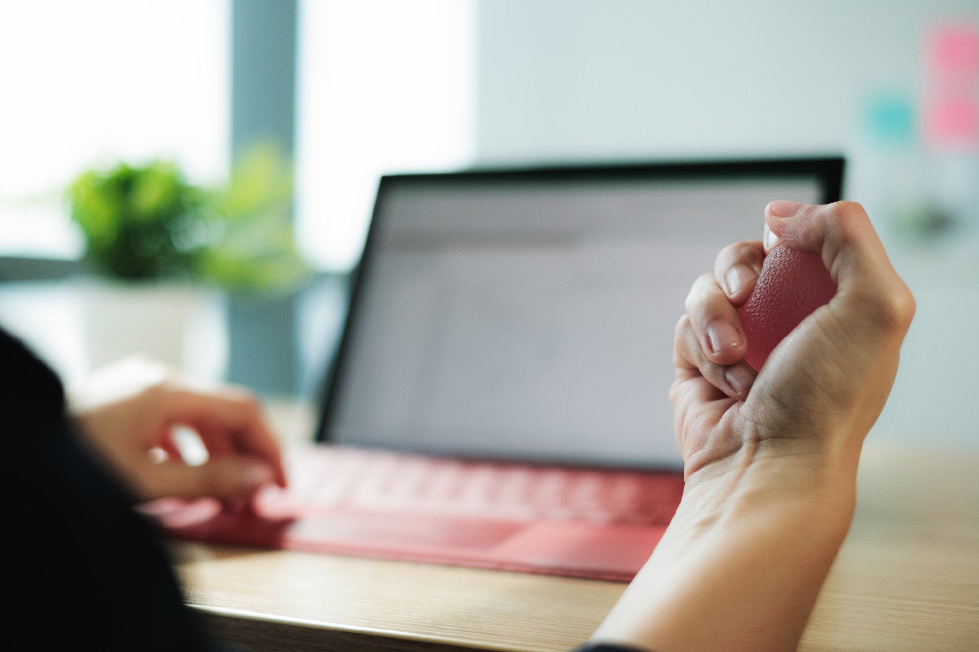 Close up of anxious white woman hands holding anti stress therapy ball at work. Female professional squeezing rubber ball as therapy for hand injury. Work related stress and rehabilitation