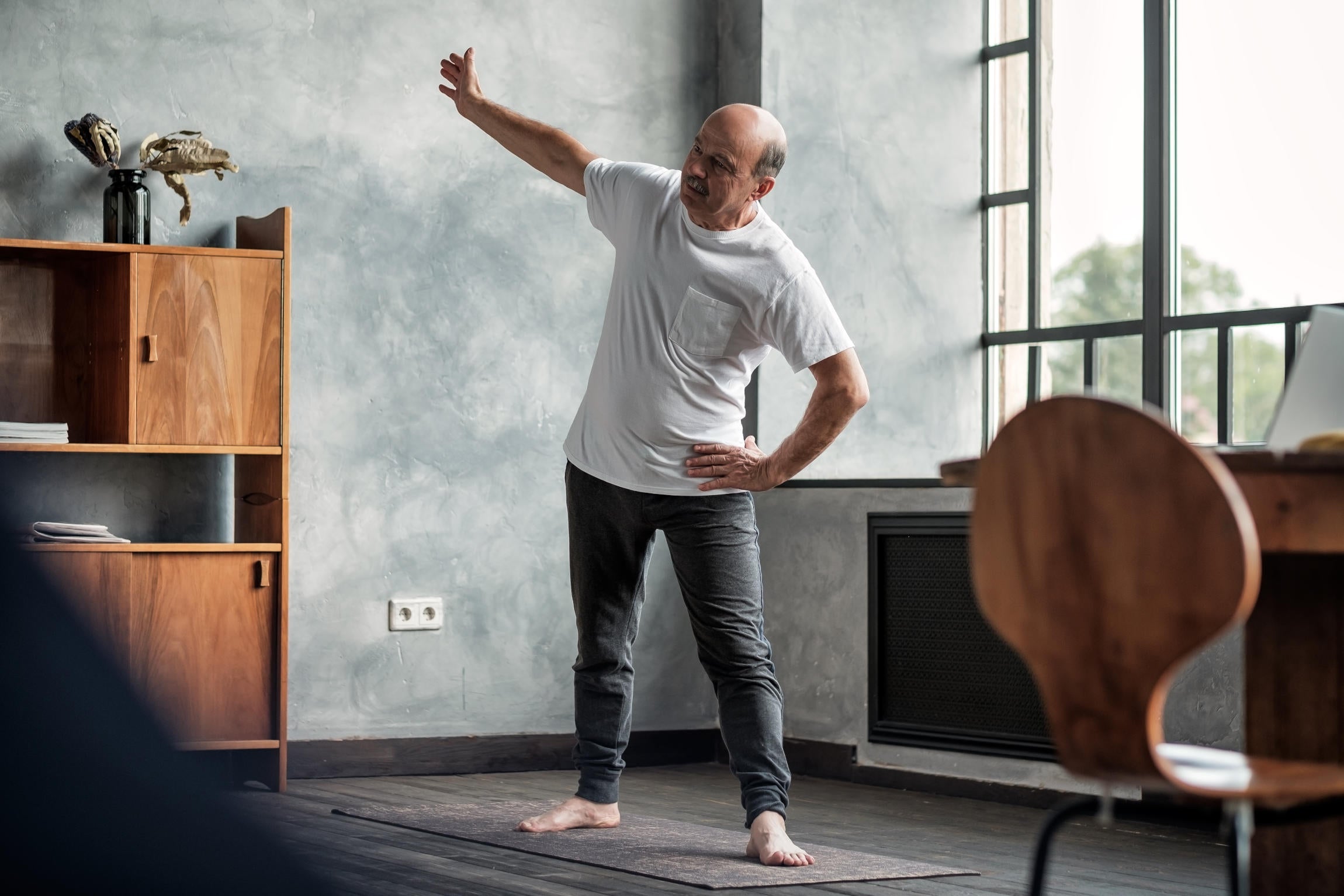 Senior hispanic man practicing yoga trikonasana pose at the living room