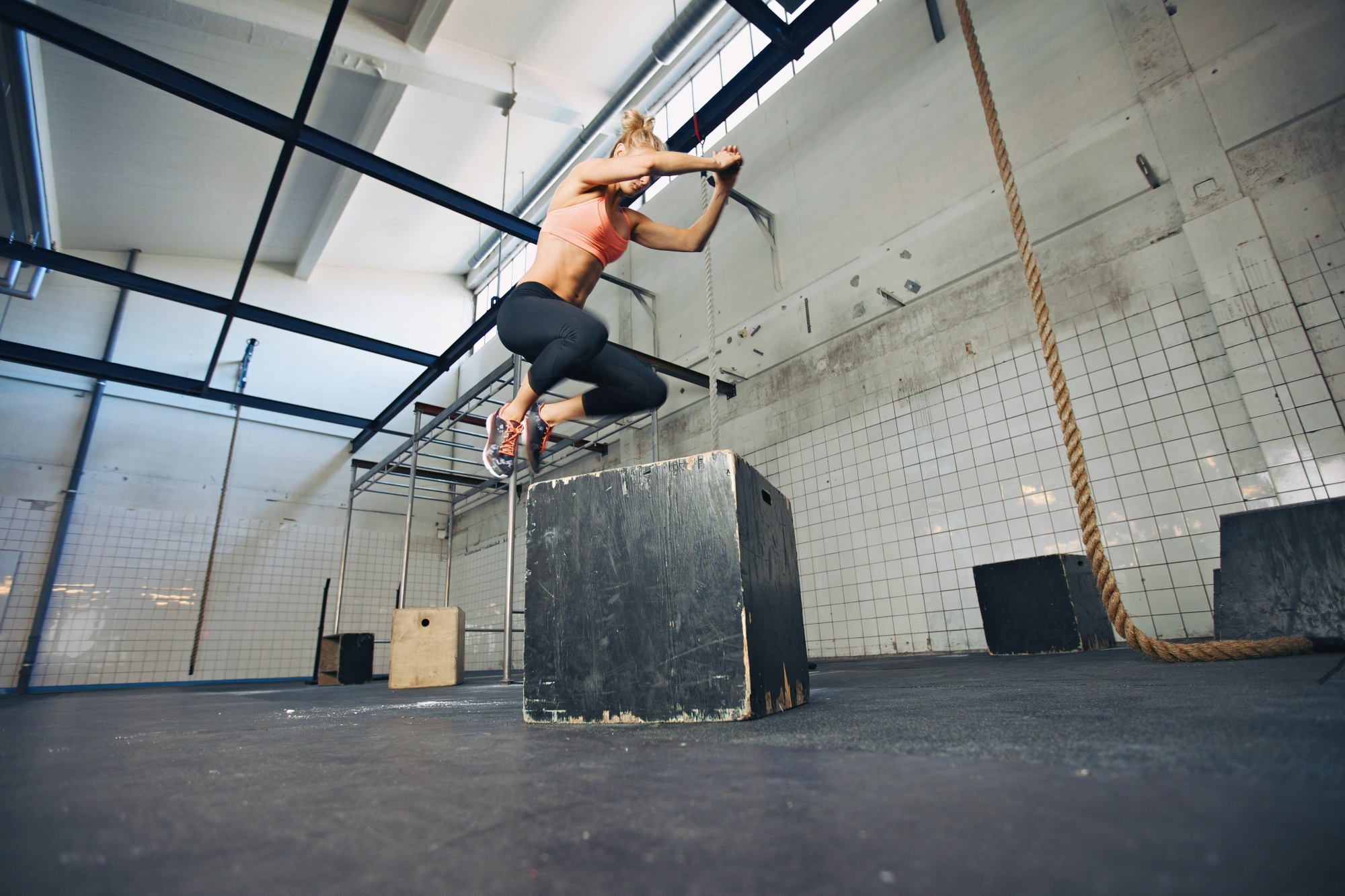 Fit young woman box jumping at a crossfit style gym. Female athlete is performing box jumps at gym.