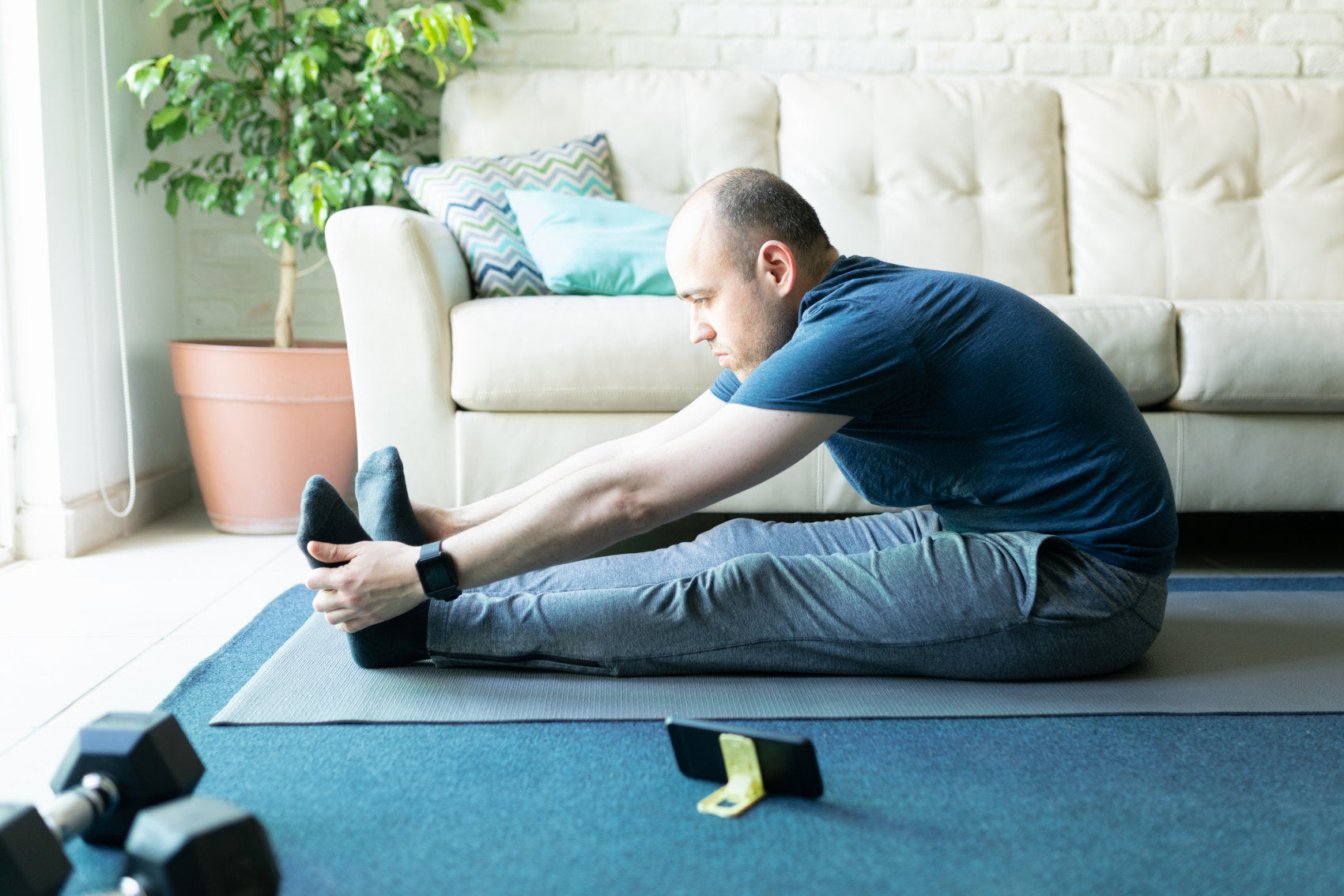 Profile view of an active man in his 30s touching his toes and stretching out while following a yoga routine on his smartphone at home