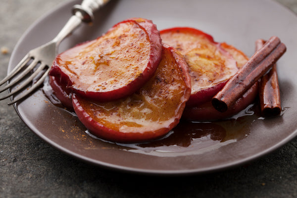 Slicked apples covered in cinnamon on a plate with cinnamon sticks and a fork.