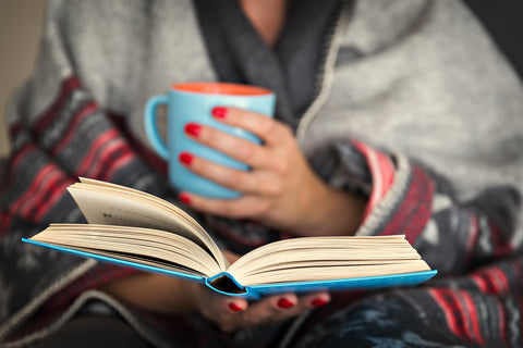 woman reading a book and holding a mug of hot beverage