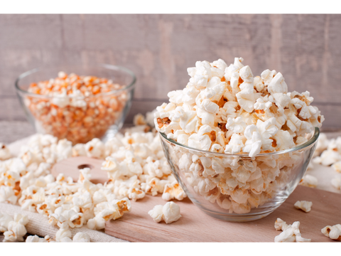 Glass bowl of microwave popcorn next to a glass bowl of popcorn seeds.