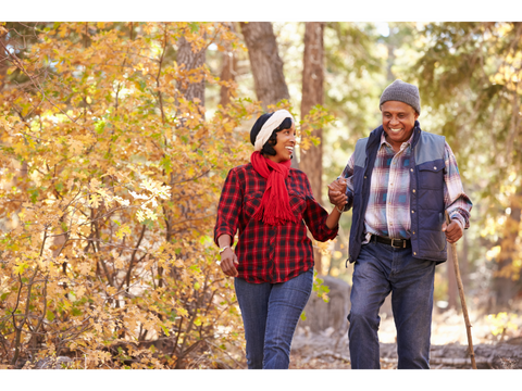 Man and woman holding hands walking outside on a trail wearing vests and scarves