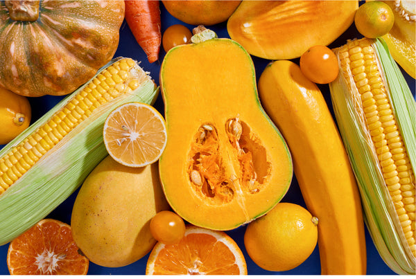 Top down view of various yellow/orange-colored foods, like corn, mango, oranges