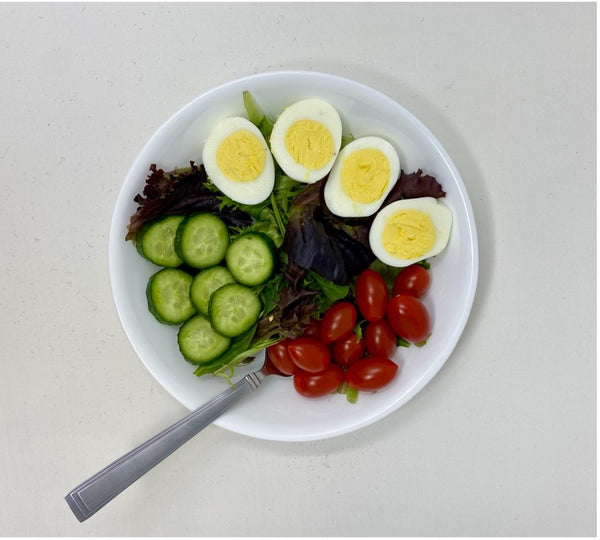 : bowl of mixed greens, cherry tomatoes, sliced cucumbers, and hard boiled eggs.