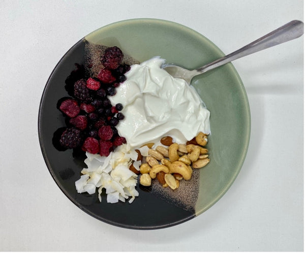 bowl of yogurt, raspberries, coconut flakes, and mixed nuts.