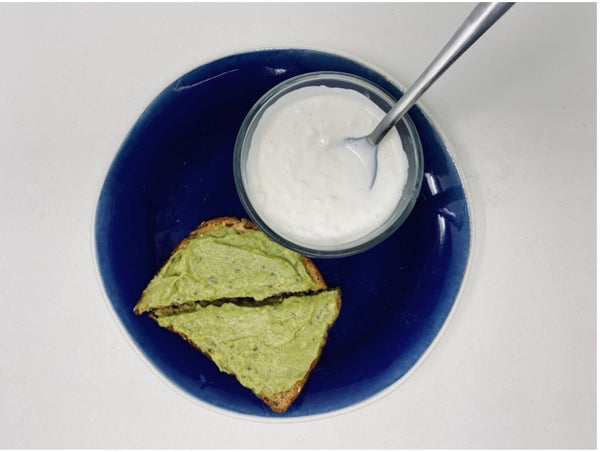 two slices of wheat bread toast with guacamole spread next to small bowl of cottage cheese on a plate.