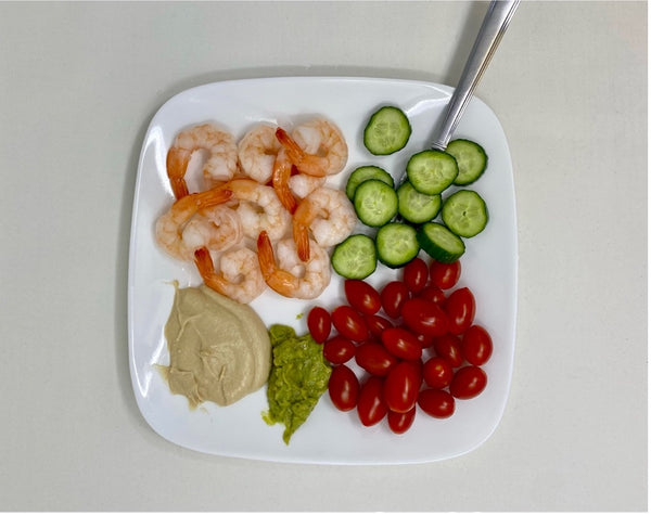 steamed shrimp, slice cucumbers, cherry tomatoes, hummus and guacamole on a plate.