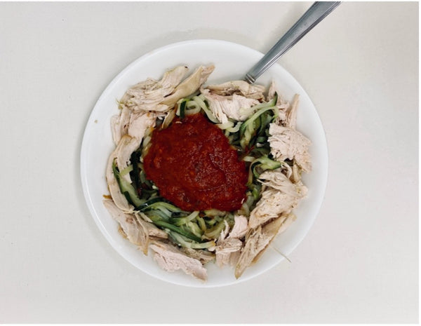 : zucchini veggie spirals and rotisserie chicken topped with pasta sauce in a bowl.