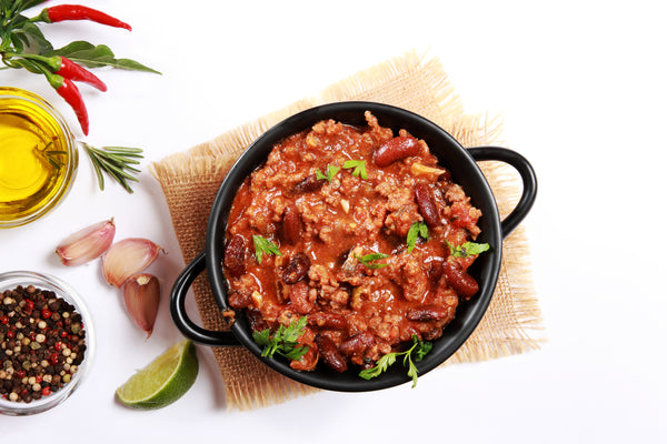 Cast-iron bowl of chili on a table with a white table cloth.