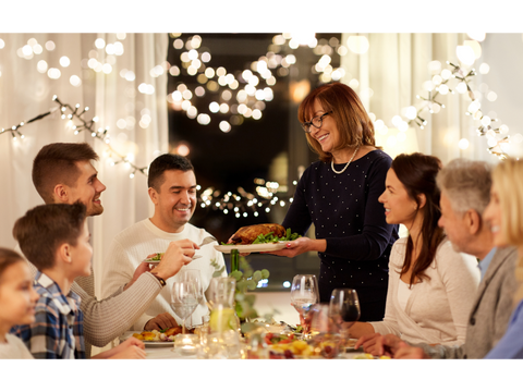 Woman bringing a plate of turkey and green beans to a festive table.