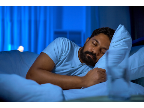 Man in a dark room with their eyes closed sleeping on a bed