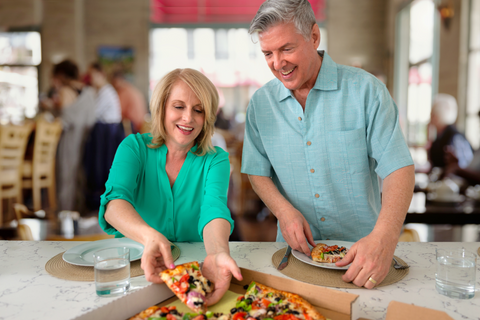 Woman at a restaurant taking a slice of thin crust, veggie pizza from a box.