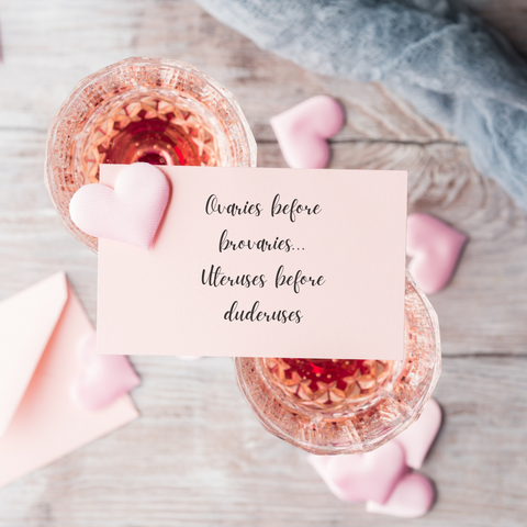 a small pink note perched on two coupe glasses of rose, seen from above. The note reads "Ovaries before brovaries... Uteruses before duderuses"