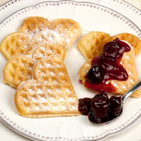 six heart shaped waffles on a white plate, half with powdered sugar, half with Lingonberries 