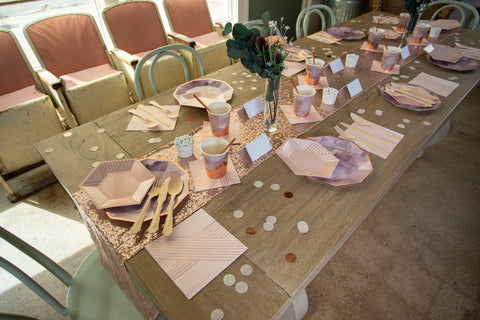 a long table in a warm light filled room with blush, rose gold, and amethyst place setting for eight and a eucalyptus arrangement at the center