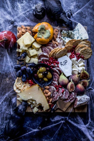 a spiderweb covered table top with a halloween grazing board of meats, cheese, olives, all fruits, and plastic rats and spiders on top
