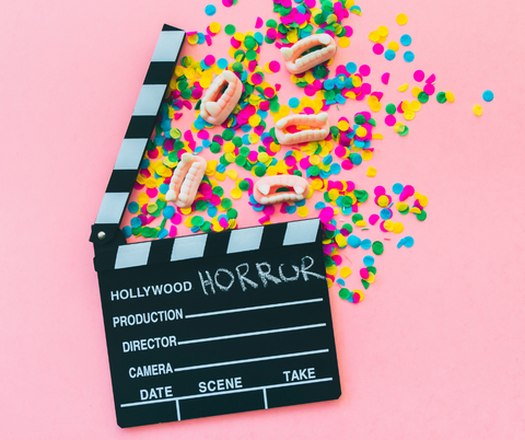 movie clapboard on pink background with rainbow confetti and gummy candy vampire fangs