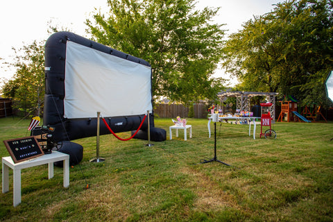 14 foot inflatable outdoor movie screen in backyard with a popcorn machine and party table set up to it's right