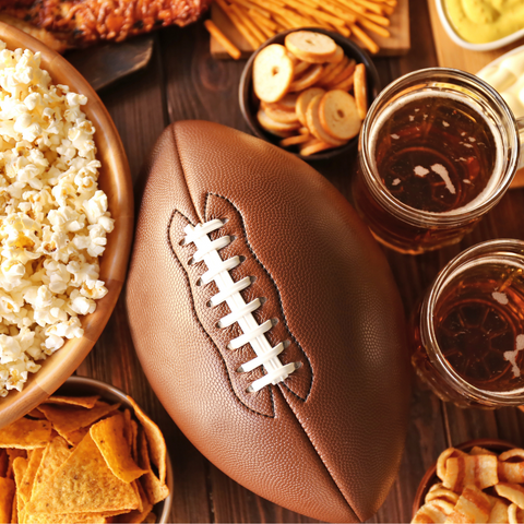 An American football sits laces up, centered on a table surrounded by bar snacks and beer