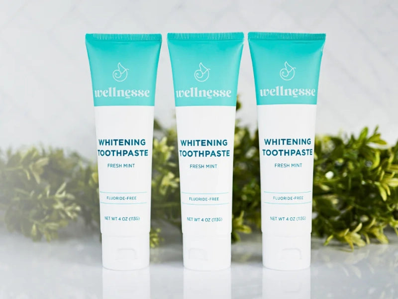 Fluoride-free toothpaste tubes standing in a row with green foliage in the background on a marble surface