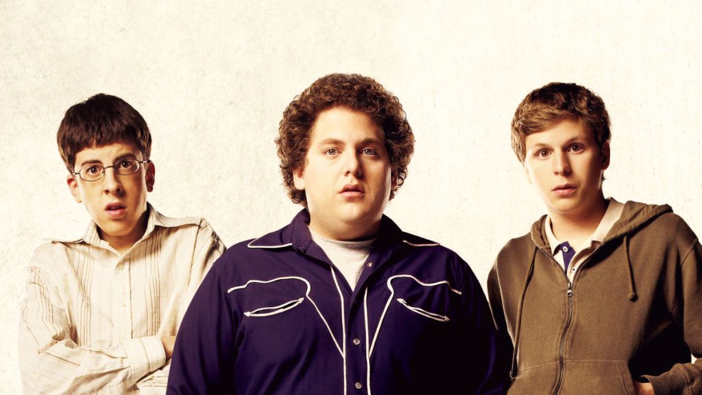 promo shot from superbad the movie. the main actors stood in a line , Mc lovin on the left wearing a white shirt with his arms crossed, the funny guys in the middle with curly hair wearing a blue shirt with white piping. and the guy from scott pilgrim on the left wearing a brown hoodie with his hands in the pcokets.