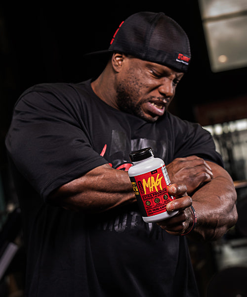 This image shows our athlete, the 2x212 Mr Olympia, simulating that he is experiencing muscle pain and he is also holding a Muscle Mag Magnesium bottle