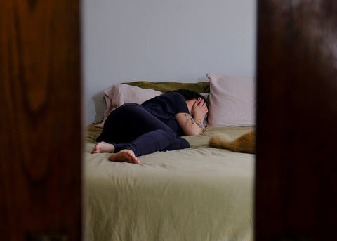 An anxious woman lies on her bed, covering her face with her hand