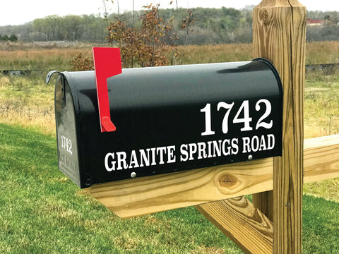 black residential mailbox with white vinyl mailbox lettering, mailbox has a red flag that is up.