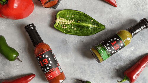 Bottles of 13 Stars hot sauce spread across a table with vegetables' around them