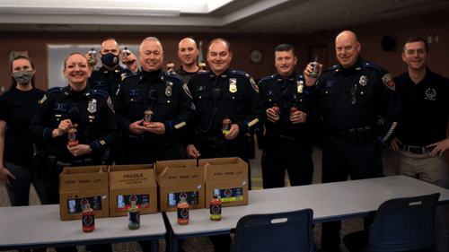 Several police officers holding up a donation of 13 Stars Hot Sauce in their barracks