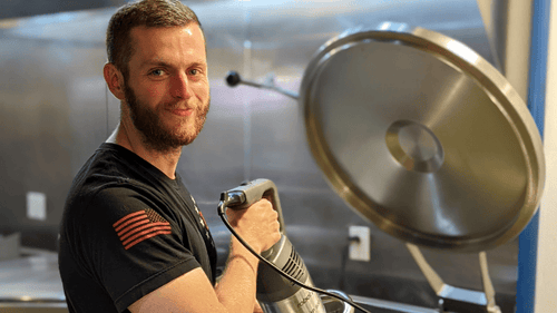 Sean from 13 Stars with a beard holding a giant immersion blender and smiling