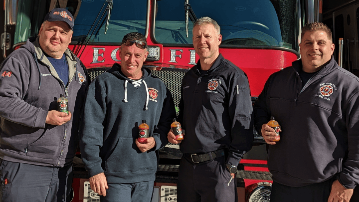 4 firefighters standing in front of a firetruck with bottles of 13 Stars hot sauce in their hands