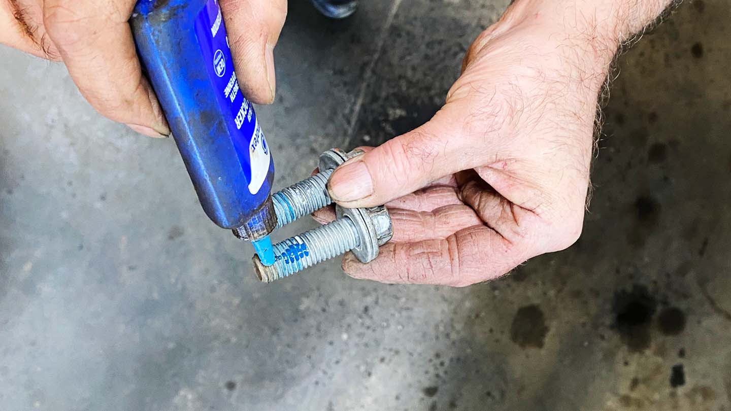 Man applying blue thread lock compound to caliper bracket mounting bolts