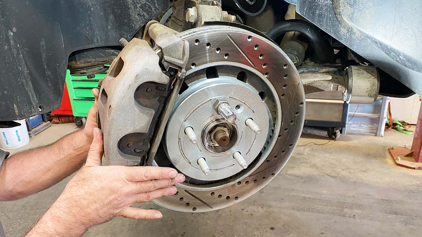 Man reinstalling caliper and bracket assembly onto car