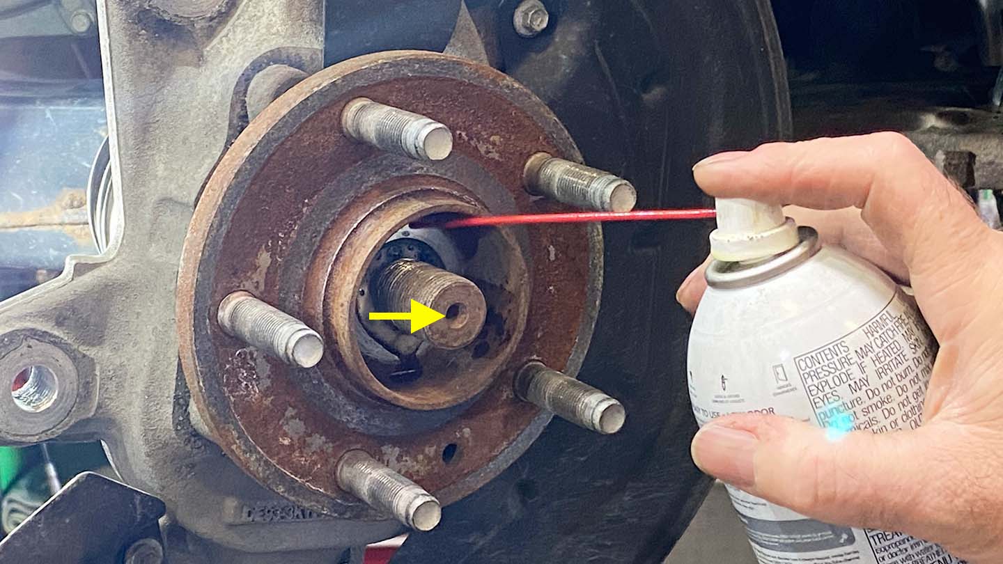 Man spraying penetrating lubricant on axle shaft