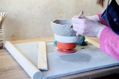 ceramics-sculptor-makes-plate-from-clay-woman-potter-working-with-clay-brush-hands-closeup-applies-pattern-product