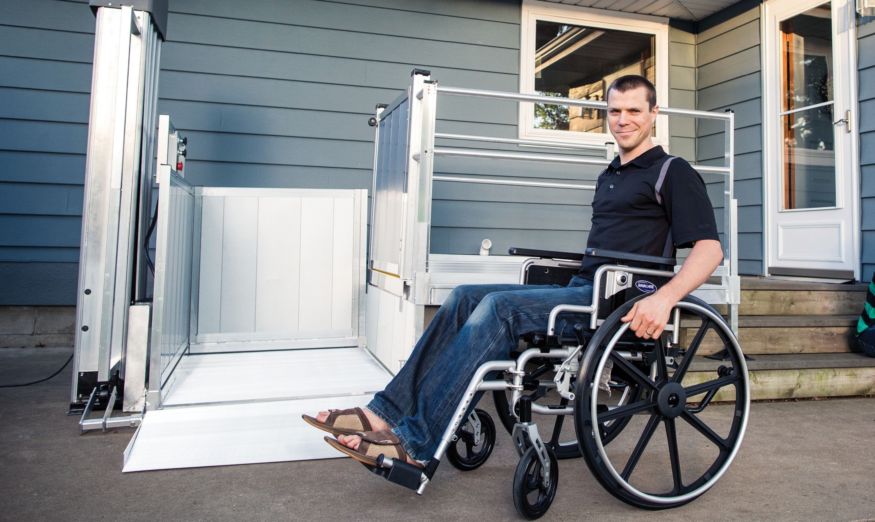 Man on wheelchair in front of PASSPORT Vertical Platform lift by EZ-Access | Wheelchair Liberty