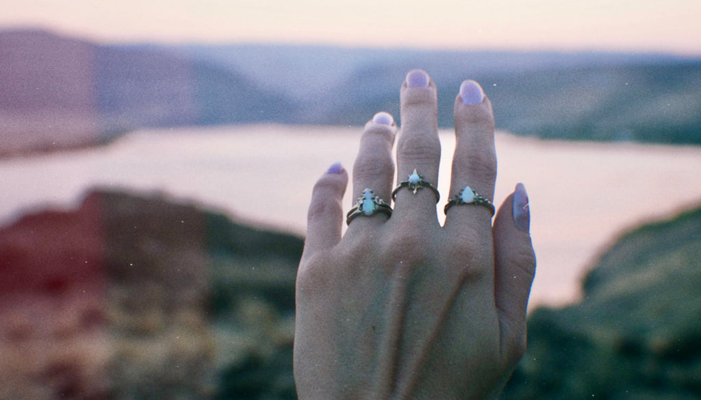 Iron Oxide Solitude Collection hand wearing three opal rings reaching towards the horizon