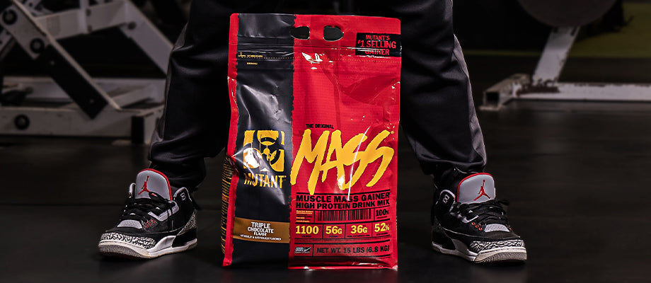 The image shows a large bag of MUTANT Mass Gainer on the gym floor with someone behind it. 