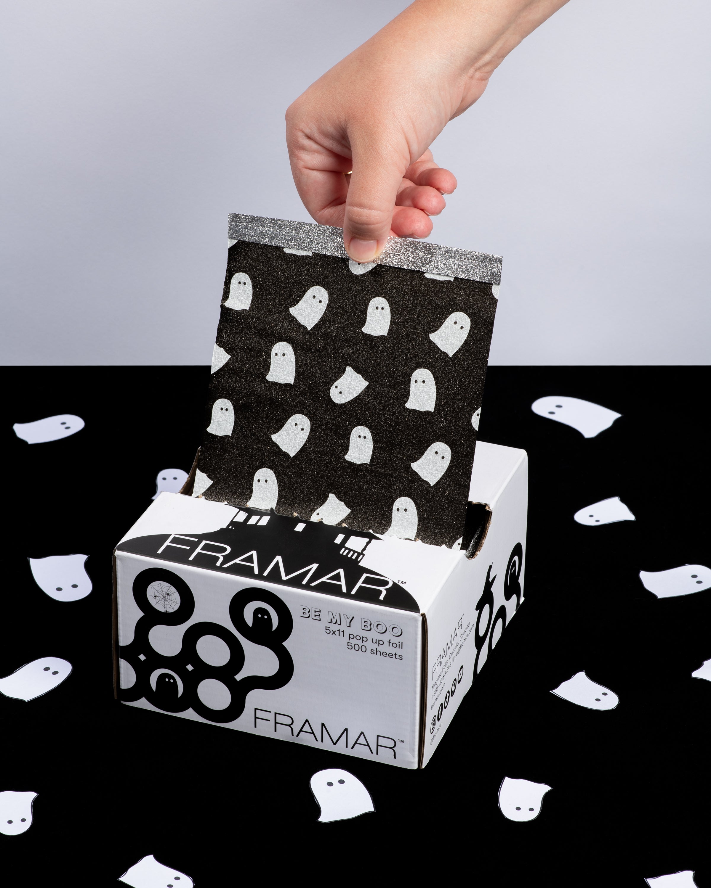 Hand pulling ghost-patterned foil from Framar box with ghost designs on a black background.