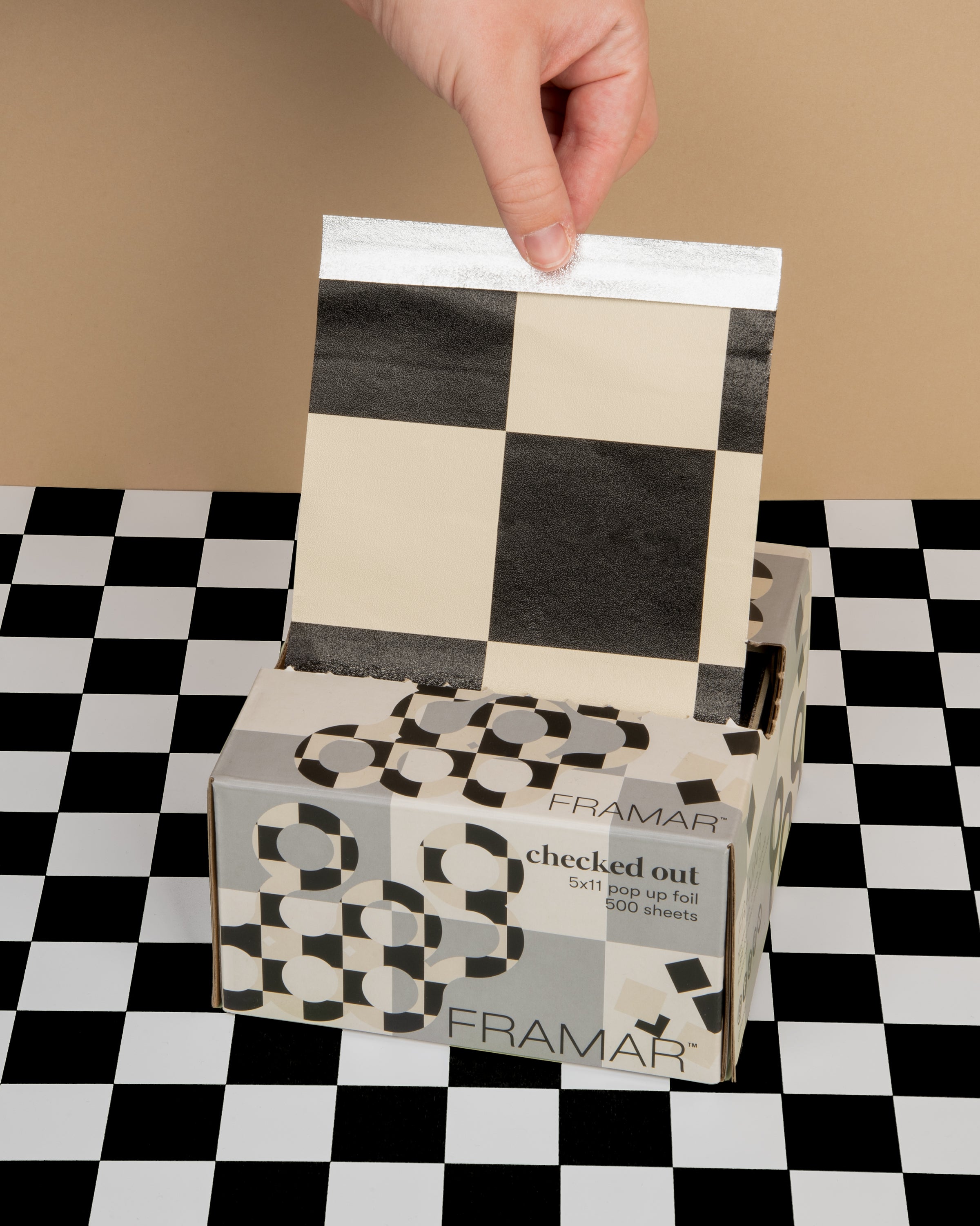 Hand pulling a sheet of foil from a patterned box on a checkered background.