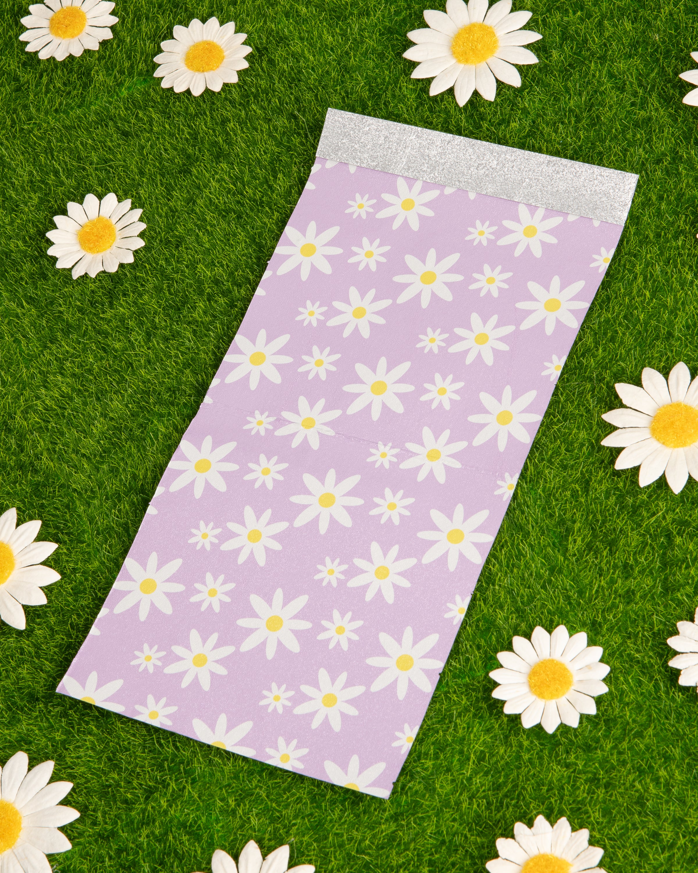 Daisy-patterned paper on grass surrounded by real daisies.