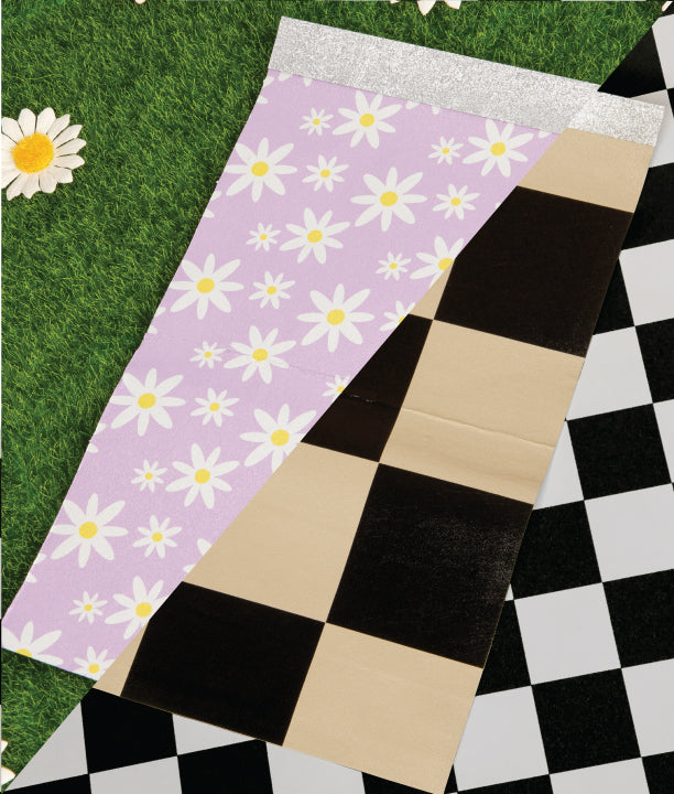 Daisy-patterned towel on a checkered background beside artificial grass with one daisy flower.