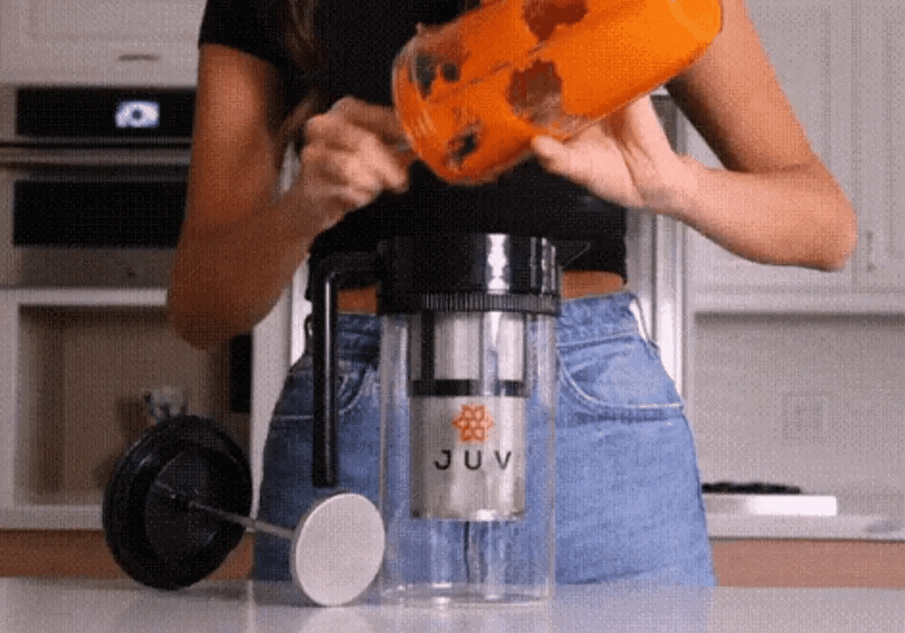 GIF of woman in bright white kitchen adding carrot blend to JUV Press and pressing out juice