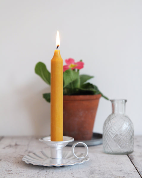 a lit yellow candle in fluted candle holder next to a glass bud vase