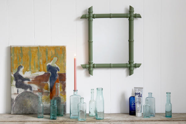 green faux bamboo mirror and a row of glass bottles