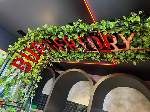 Metal Arch with the Burgertory logo decorated with artificial hanging plants